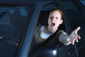 An angry young female driver in her car shouting through the window and hitting the horn