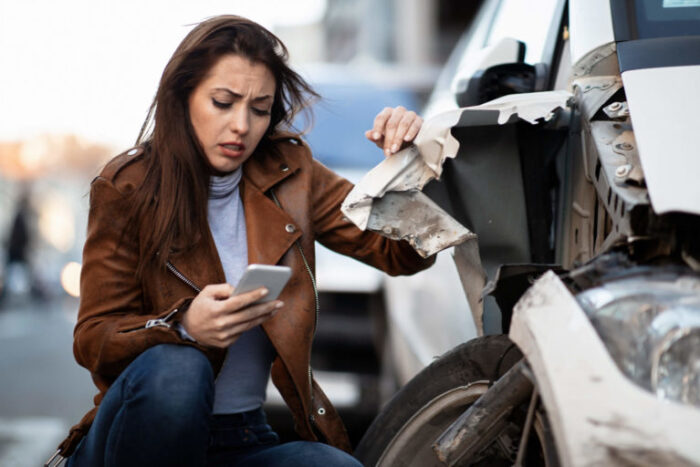 woman on phone next to car that has been in an accident